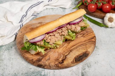 Tuna sandwich on wood serving board. Sandwich made with tuna meat, special sauce, purple onion, pickles and greens clipart