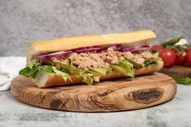 Tuna sandwich on wood serving board. Sandwich made with tuna meat, special sauce, purple onion, pickles and greens clipart