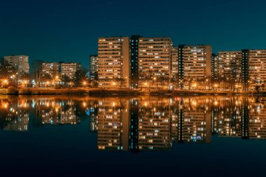 Night view on Tysiaclecie estate in Katowice, Silesia, Poland. Lightened residential buildings with surrounding trees at dusk seen through the lake. 