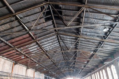 Gable roof truss of a large, vintage factory hall. Roofing construction (sheathing) made of wooden planks. Brick walls and arcade windows. Industrial interior.