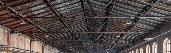 Gable roof truss of a large, vintage factory hall. Roofing construction (sheathing) made of wooden planks. Brick walls and arcade windows. Industrial interior.