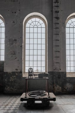 Eski bir fabrikada yüksek bir atari salonu penceresi. Paslı, endüstriyel alan, kirli duvarlar ve tarihi döşemeler. Eski moda bir kablo işleme makinesi ve kablo bobini olan eski metal bir araba..