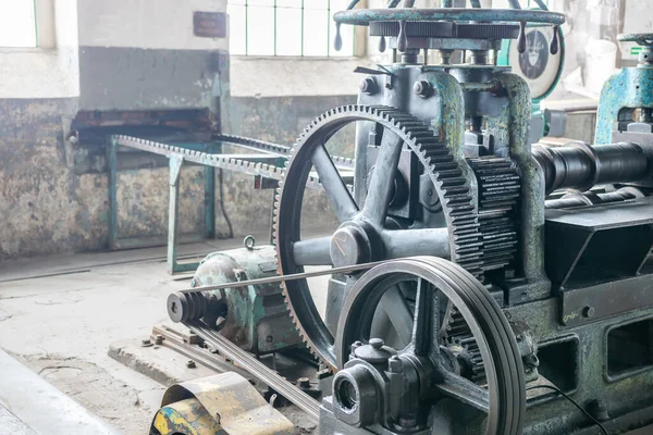 Old-fashioned rolling mill machine in historical factory. Original equipment from the beginning of the XX century. Big gear, rolls and other parts of the machine. Rusted walls in the background.