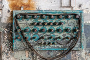 Several used factory machine v-belts hanging on colorful, damaged table with hangers. Shabby wall in the background. Part of an old factory's equipment.