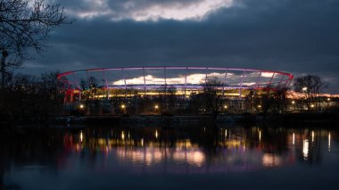 Chorzow, Polonya - 8 Şubat 2023: Chorzow 'daki Silesian Park. Akşamları Silezya Stadyumu. Aydınlatılmış stadyum yapısı. Önplanda göl.