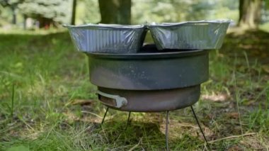 Parktaki çimlerin üzerine yayılmış küçük paslı ızgara. Mükemmel bir açık hava ızgarası. Izgarada, içinde yiyecek olan iki alüminyum tepsi.