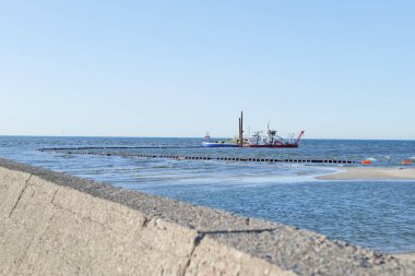 Denizci Baltık Denizi 'nin dibini tarıyor. Güneşli bir yaz gününde tayfayla birlikte iki dredger gemisi iş başında. Ön plandaki iskelenin beton astarı. Leba, Polonya. 