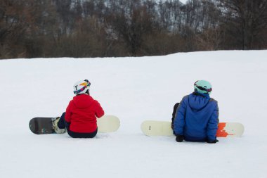 Karlı bir yamaçta oturan iki snowboardcu