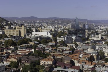 Hareketli şehir Tiflis, açık gökyüzü altında modern ve geleneksel mimarinin bir karışımını ortaya çıkarıyor. Renkli çatılar gökyüzü ile tezat oluşturarak, davetkar bir şehir manzarası yaratıyor..