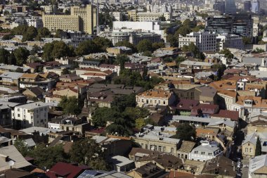 Renkli çatılar Tiflis 'in ufuk çizgisini doldurarak modern binaları parlak mavi bir gökyüzü altında geleneksel Gürcistan mimarisiyle harmanlıyor. Sahne, şehrin eşsiz cazibesini ve canlılığını yakalıyor..