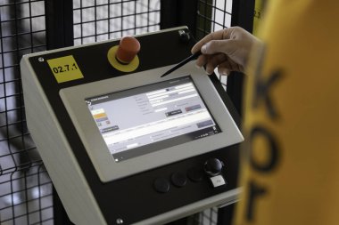 Bir birey endüstriyel ortamda kontrol paneliyle etkileşime geçiyor. Dokunmatik ekran çeşitli işletim ayarlarını görüntüler ve ekipmanları etkin bir şekilde kontrol eder.