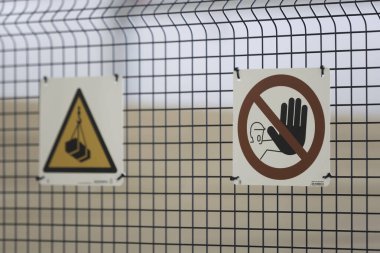 İnşaat alanındaki tel örgülerde iki güvenlik işareti var. Biri düşen nesneler hakkında uyarırken, diğeri izinsiz personel girişini yasaklıyor..
