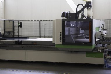 Yüksek teknolojili bir CNC makinesi geniş bir imalat tesisinde çalışır ve ahşap malzemelerini verimli bir şekilde kesip şekillendirme yeteneğini gösterir. Modern düzende üretimde kesinlik vurgulanıyor..