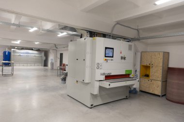 Ahşap işleme için tasarlanmış yüksek teknolojili zımpara makinesi olan geniş bir atölye. Mekan iyi aydınlatılmış ve organize, modern ekipmanlar sergileniyor ve temiz bir çalışma ortamı var..