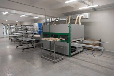 Bu atölyede, verimli bir iş akışı için düzenlenmiş birden fazla raf ünitesi eşliğinde, işleme malzemeleri için tasarlanmış büyük bir endüstriyel makine sergileniyor. Mekan iyi aydınlatılmış ve düzenlenmiş..