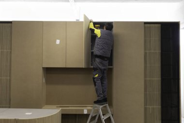 Yetenekli bir işçi çağdaş bir iç mekanda dolaplar kurmak için merdiven kullanır. Olay yeri gün ışığıyla aydınlandı. Detaylara dikkat çekiyor..