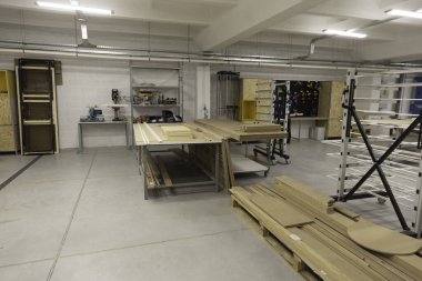 Parlak ve temiz atölye, ahşap işçiliği için düzgün düzenlenmiş alet ve malzemeler içerir. Çalışma alanı, verimli proje çalışması için birden fazla çalışma tablosu ve depolama çözümleri sergiliyor.