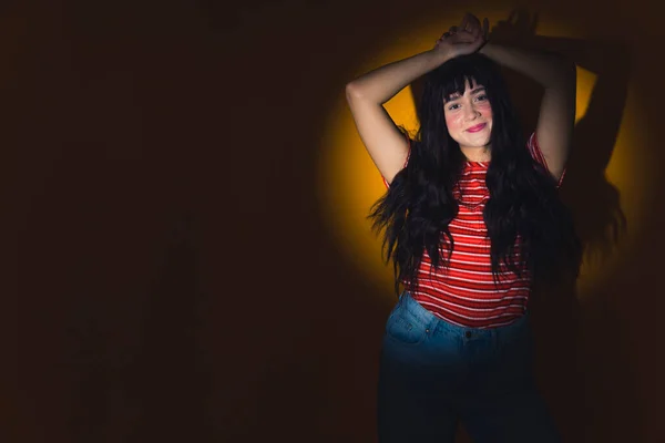 cowboy shot of a pretty and lovely Caucasian girl with long dark hair holding hands on the head and smiling, circle light photoshoot copy space. High quality photo