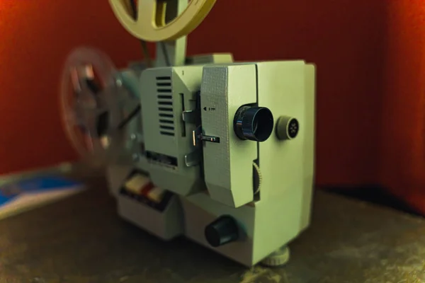 Old cinematography concept. Antique vintage film projector. Closeup indoor shot. Red blurred background. Hobbies and industry. High quality photo