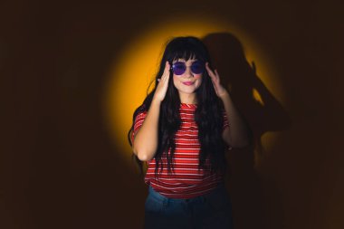 Çember ışıklarında duran, güneş gözlüklerine dokunan, orta boy, koyu renk saçlı, beyaz bir kız. Yüksek kalite fotoğraf