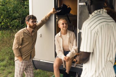 20 'li ya da 30' lu yaşlarda farklı etnik gruplar kampçılarının önünde duruyor, konuşuyor, yeni bir gezi planlıyor ve kaynaşıyorlar. Açık hava çekimi. Yüksek kalite fotoğraf