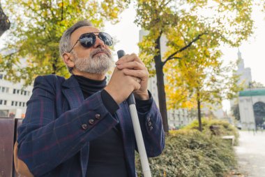 Elinde bastonla yürüyen güneş gözlüklü, zarif, kör sakallı, gri saçlı olgun bir adam. Parkta sonbahar sezonunun tadını çıkarıyor. Yüksek kalite fotoğraf