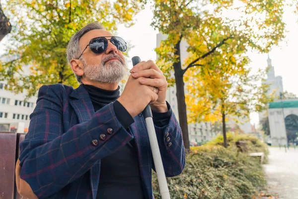 stock image Elegant blind bearded grey-haired mature man with dark sunglasses on holding a walking stick, enjoying fall season in the park. High quality photo