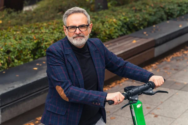 stock image Millennial modern bearded grey-haired mature man with eyeglasses on posing, standing with an electro scooter in the park alley. High quality photo