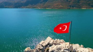 Türkiye 'deki turkuaz Oymapinar Gölü' nün kayalık kıyı bölgesinde canlı kırmızı Türk bayrağı. Yaz mevsiminde gidilecek yerler. Güzel güneşli hava, mükemmel koşullar. Yüksek kalite 4k görüntü