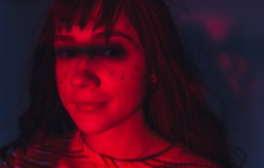 Yüzünde çil şeklinde kristaller ya da mücevherler olan ikili makyaj sanatçısı olmayan genç birinin portresi. Yüzü kırmızı ışıkla aydınlanmış, her iki gözünde de gölge var. Yüksek kalite fotoğraf