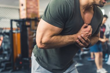 Tanımlanamayan beyaz, yeşil gri tişörtlü vücut geliştiren erkek spor salonunda kol kaslarını sıkıyor. Arka plan bulanık. Yüksek kalite fotoğraf
