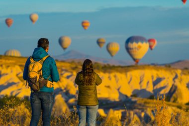 10.11.2022 Kapadokya, Türkiye. Bir çift siyah saçlı turistin sabahları sıcak hava balonlarının muhteşem panoramik manzarasını izlemesi. Yüksek kalite fotoğraf