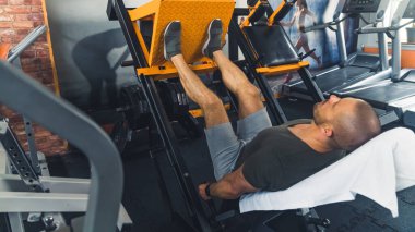 Orta yaşlı, kaslı, gri elbiseli en sevdiği spor salonunda bacak egzersizi yapıyor. Düzenli çalışmanın faydaları. Vücut kasları gelişiyor. Yüksek kalite fotoğraf