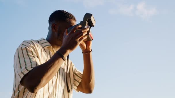 年轻的黑衣人穿着条纹衬衫 用老式即时摄像相机给朋友拍照 横向室外视频 高质量的4K镜头 — 图库视频影像