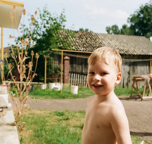 Square analog analog photo of a young five or six-year-old blond caucasian boy without a t-shirt enjoying his summer holidays at the countryside circa 1995. High quality photo