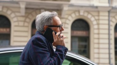 Yakışıklı ve kendine güveni olan gri saçlı iş adamı işe giderken telefonla konuşuyor. Yüksek kalite 4K görüntü
