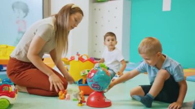 Genç beyaz bir öğretmen ve yerde oturan sarışın bir çocuk ve anaokulundaki diğer oyuncaklarla oynuyorlar. Yüksek kalite 4k görüntü