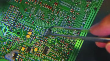 Mikroçiplerin PCB 'nin yüzeyine elle montajı. Büyüteçle vurulmuş. Tanımlanamayan beyaz birinin cımbızıyla. Yüksek kalite 4k görüntü