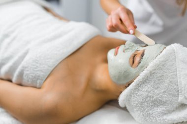 SPA günü ve rahatlama konsepti. Derin cilt temizliği. Asyalı bayan müşterisinin yüzüne kilden maske takan tanınmamış Kafkas güzellik uzmanı. Yüksek kalite fotoğraf