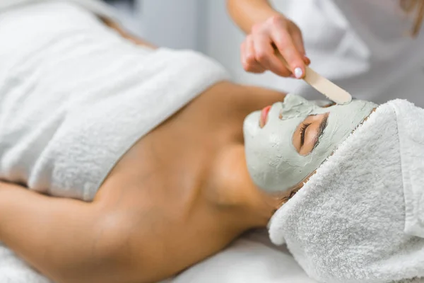 stock image SPA day and relaxation concept. Deep skin cleanse. Unrecognizable caucasian beautician spreading clay mask onto the face of her Asian female client. High quality photo