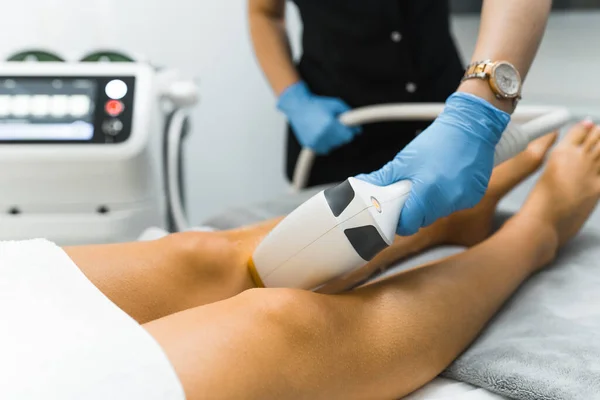 SPA and Beauty Salons treatment - laser hair removal from legs. Unrecognizable caucasian beautician in protective blue gloves using laser on her caucasian client. Hair removal cosmetology procedure