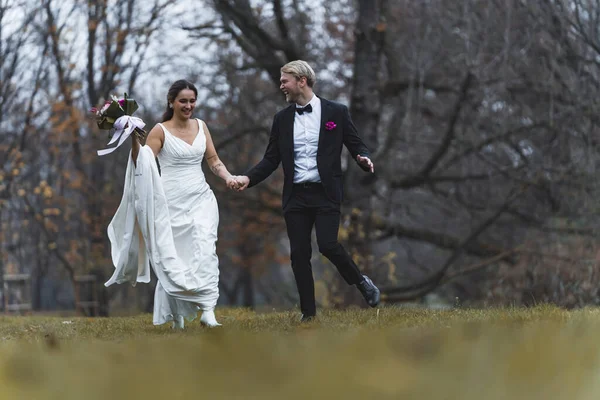 异性恋新婚夫妇的全长户外拍摄 异族通婚概念 身着黑色西服的斯堪的纳维亚新郎和他美丽的土耳其新娘在森林的林间空地上奔跑 高质量的照片 — 图库照片