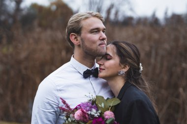 Yeni evlilerin saf aşkı. Evlilik töreninden sonra genç bir çiftin orta boy yakın portresi. Karısı ona sarılırken İskandinav yakışıklı damat ileriye bakıyor. Arka planda alan var. Yüksek