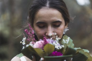 Ortadoğulu güzel kahverengi saçlı gelinin düğün buketinin renkli çiçeklerini koklayan portresi. Arka plan bulanık. Açık havada Photoshoot 'la evlendi. Yüksek kalite fotoğraf