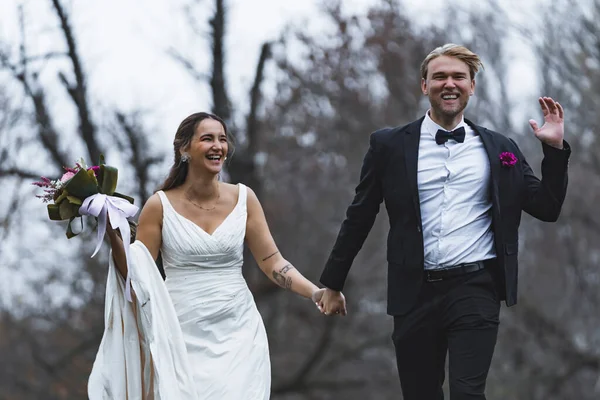 新婚夫妇快乐地跑来跑去 欢笑着 室外森林秋天摄影 土耳其新娘穿着无袖婚纱 与优雅英俊的斯堪的纳维亚丈夫牵着手 高质量的照片 — 图库照片