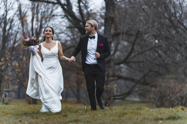 Late autumn wedding ceremony. Full-length shot of two people - Middle Eastern ethnic woman in white wedding gown holding the hand of her newlywed Scandinavian husband. Positive memories. High quality