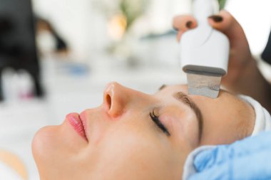Aşırı yakından görülen mikro dermabrüksiyon SPA prosedürü. Uzun siyah kirpikleri olan orta yaşlı beyaz bir kadının yüzünde kullanılan özel kozmetik aletler. Arka plan bulanık. Yüksek kalite