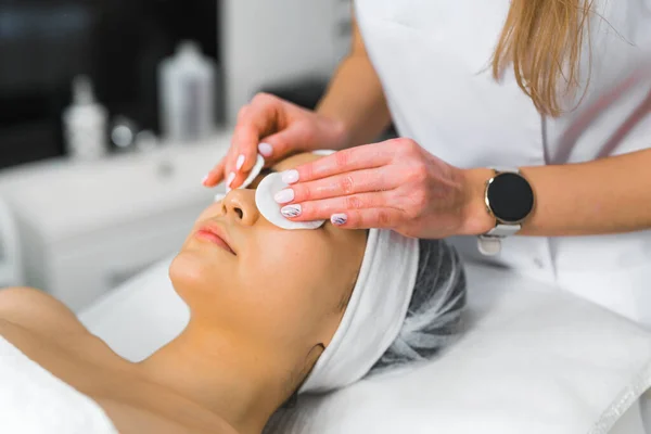 Cleansing facial at SPA facility. Young beautiful Asian woman lying down on SPA bed with protective headband on her hair during eye-relaxing procedure. High quality photo
