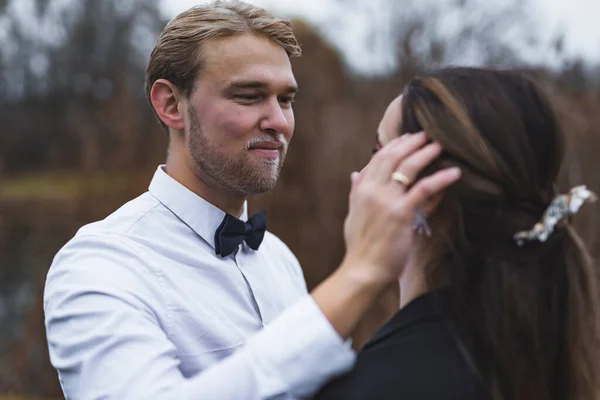 stock image Attractive well-build blond bearded Scandinavian groom gently touching his newlywed wifes long, brown hair. Blurred background. Autumn photoshoot. High quality photo