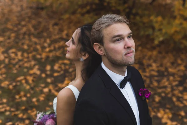 金秋结婚的日子 严肃的斯堪的那维亚新郎穿着正式的衣服 与他的土耳其新娘背靠背地站着 秋天公园的摄影 高质量的照片 — 图库照片